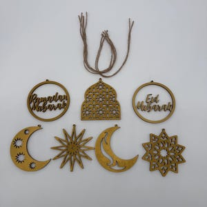 May include: A collection of wooden Ramadan and Eid Mubarak decorations. The set includes crescent moons, stars, and circular ornaments with text. The pieces are in a warm, golden color and are connected with twine for hanging.