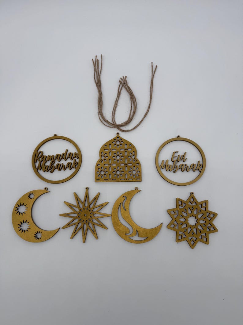 May include: A collection of wooden Ramadan and Eid Mubarak decorations. The set includes crescent moons, stars, and circular ornaments with text. The pieces are in a warm, golden color and are connected with twine for hanging.