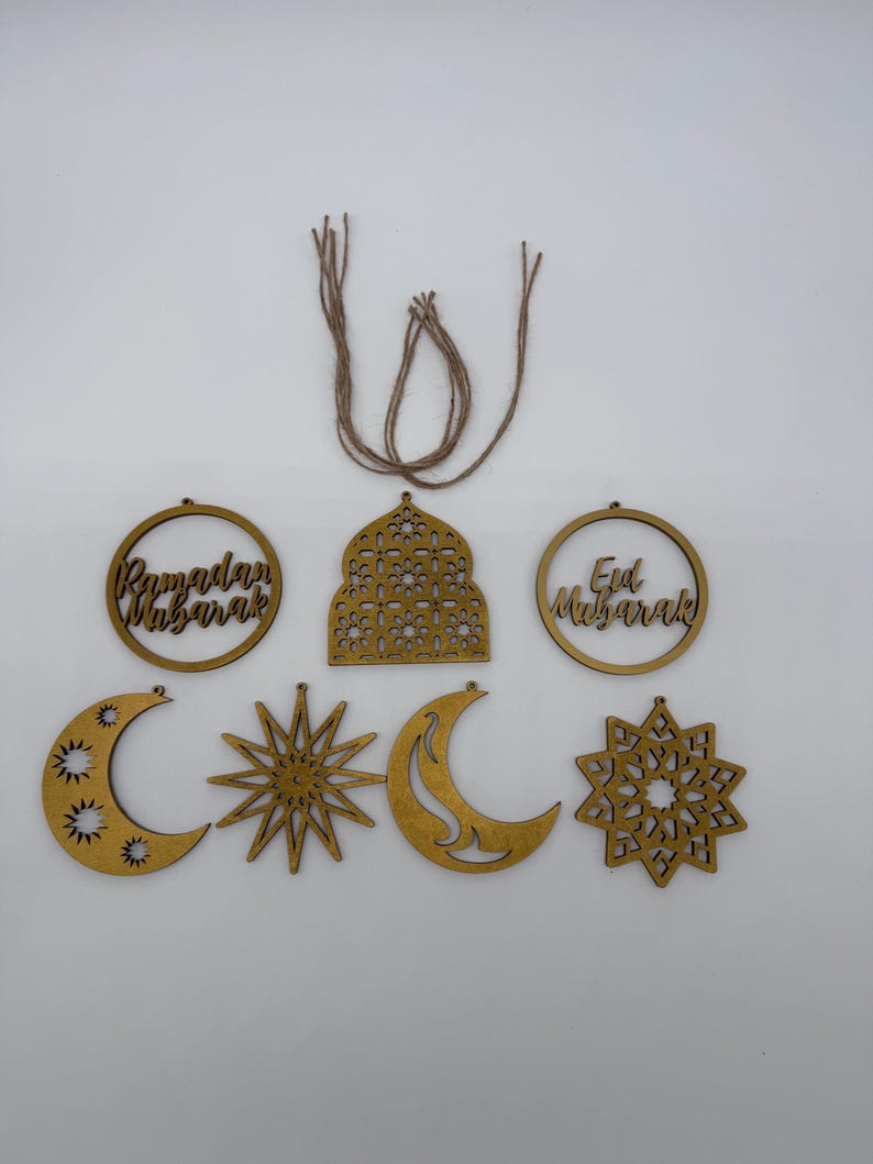 May include: Wooden Ramadan and Eid Mubarak ornaments in various shapes, including crescent moons, stars, and circular frames. The ornaments are light brown with intricate cut-out designs and include twine for hanging.