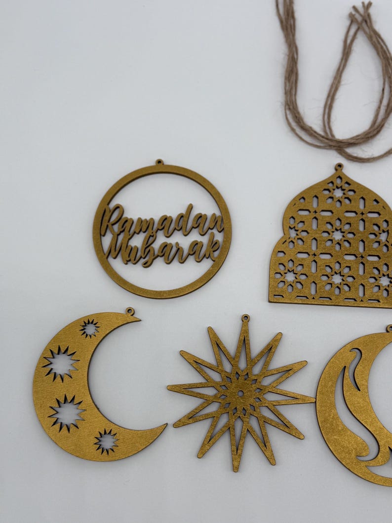 May include: Wooden Ramadan Mubarak decorations in various shapes, including a crescent moon, star, and a circular frame with the words "Ramadan Mubarak." The decorations are a light brown color and are designed to be hung.