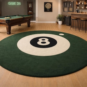 May include: A round green rug with a large white circle and a black number 8 in the center. A smaller white circle is in the upper right. The rug is on a hardwood floor, with a pool table and bar in the background.