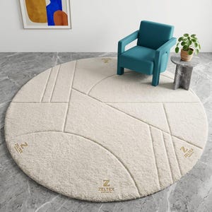 May include: A large, round, cream-colored area rug featuring a textured, geometric pattern of raised lines. The rug displays the gold-colored logo ZELTEX EXPORTS in three distinct locations across its surface, showcasing a plush, tufted pile construction.