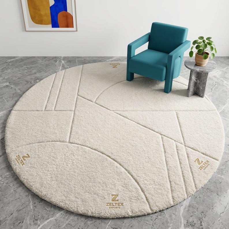 May include: A large, round, cream-colored area rug featuring a textured, geometric pattern of raised lines. The rug displays the gold-colored logo ZELTEX EXPORTS in three distinct locations across its surface, showcasing a plush, tufted pile construction.