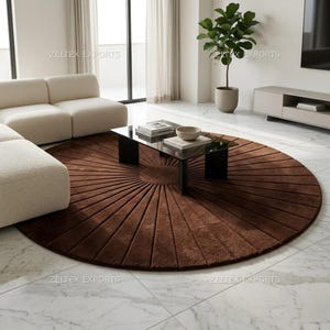 May include: A large, circular, dark brown area rug featuring a sunburst pattern of raised, linear tufted sections radiating from a solid center. The rug is positioned on a white marble floor, with the text ZELTEX EXPORTS visible in the image.