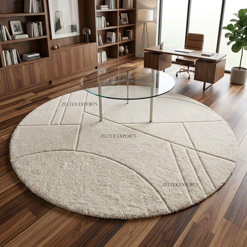 May include: A large, round, cream-colored area rug featuring a textured surface with carved geometric lines and patterns. The rug displays the text ZELTEX EXPORTS in three separate locations across its surface, set against a dark wood floor.
