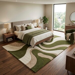 K&ouml;nnte beinhalten: Ein rechteckiger Teppich mit einem wellenf&ouml;rmigen, abstrakten Muster in Olivgr&uuml;n, Creme und Beige. Der Teppich hat eine dicke, flauschige Textur und liegt auf einem dunklen Holzboden, der sich unter einem Bettgestell in den Raum erstreckt.