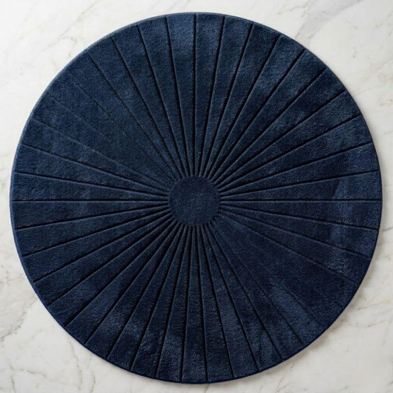 May include: A circular navy blue rug featuring a textured sunburst pattern with raised lines radiating from a solid center circle to the outer edge. The rug has a soft, plush appearance and a consistent deep blue color throughout its surface.
