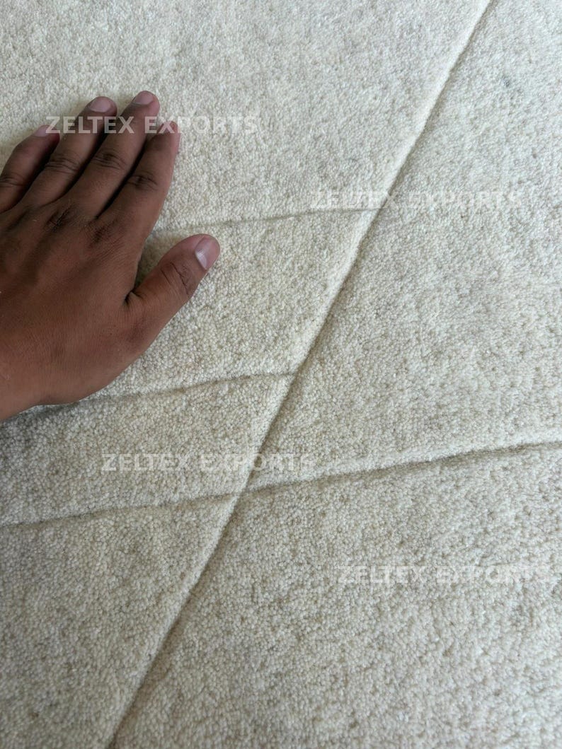 May include: A cream-colored area rug with a thick, plush, tufted texture featuring diagonal carved lines that create geometric sections across the surface. The text ZELTEX EXPORTS is printed in a light font across the rug's surface.