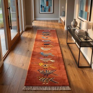 May include: A long, rectangular, burnt-orange runner rug featuring a series of stylized, multi-colored birds arranged in a vertical row. The rug has a fringed edge at both ends and includes the text ZELTEX EXPORTS printed across the center.