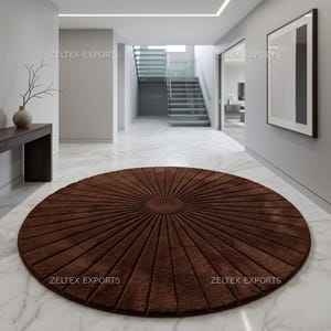 May include: A circular brown rug featuring a radial sunburst pattern with textured, raised lines extending from a solid center circle. The rug is positioned on a white marble floor in a hallway. The text ZELTEX EXPORTS appears on the image.