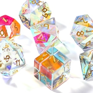 May include: A collection of iridescent polyhedral dice with gold-colored numbers. The dice are various shapes, including D20s and D6s, and feature a colorful, prism-like effect. The dice are set against a white background.
