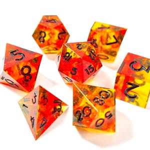 Op de afbeelding: Set van zeven polyhedrale dobbelstenen met een vurige rode en gele kleurstelling. Elke dobbelsteen heeft zwarte cijfers en een glinsterend, doorschijnend uiterlijk. Ideaal voor tabletop gaming.