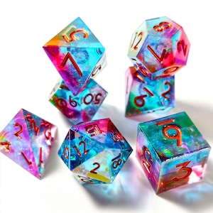 May include: A set of colorful, gemstone-like dice with red numbering. The dice are a mix of blue, purple, pink, and yellow, with a translucent appearance. The set includes various shapes, including a six-sided die, a ten-sided die, and a twelve-sided die.