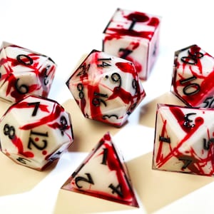 Puede incluir: Un conjunto de dados poliédricos con una base blanca y un diseño de salpicaduras rojas. Los dados incluyen varias formas, como d4, d6, d8, d10, d12 y d20. Cada dado tiene números negros.
