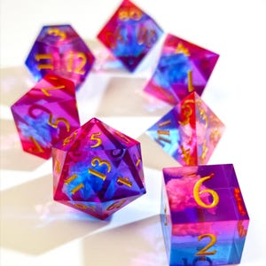 May include: A collection of seven multi-sided dice in shades of purple, pink, and blue, with gold numerals. These dice are designed for role-playing games and are in various geometric shapes.