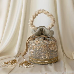 May include: A gray velvet drawstring bag with gold embroidery and a beaded handle. The bag features floral and leaf patterns, with a beaded border and tassel accents. The handle is made of white pearls.