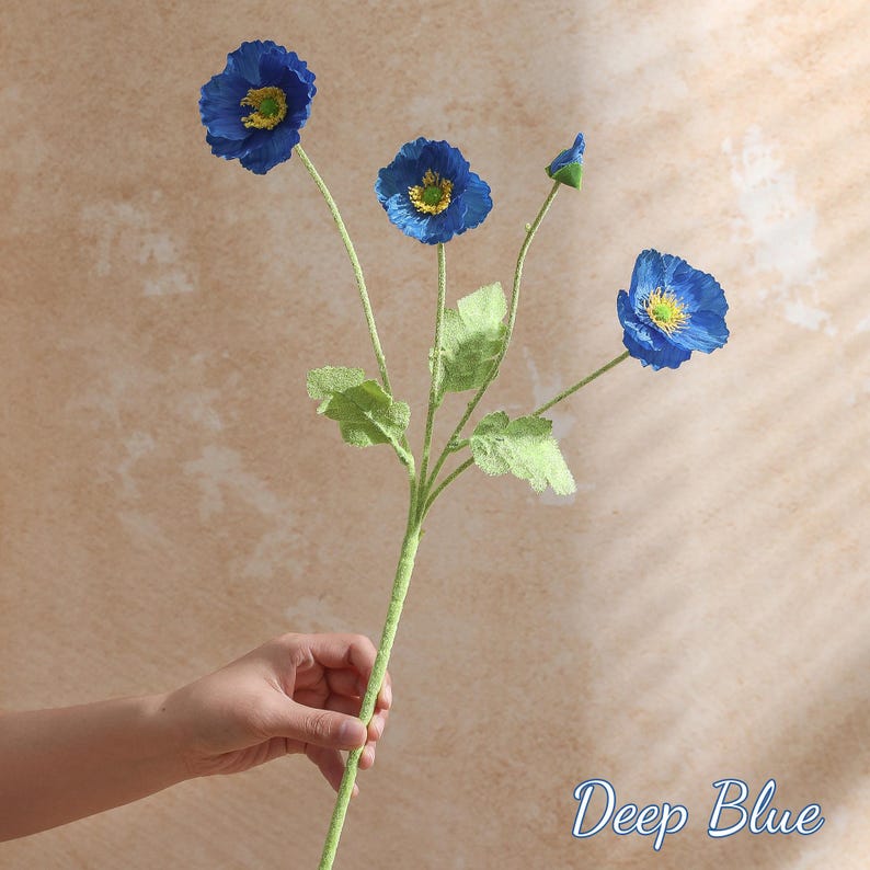 May include: A deep blue artificial poppy stem with four flowers and green leaves. The flowers have yellow centres and are in various stages of bloom. The stem is green and the text "Deep Blue" is in the bottom right corner.