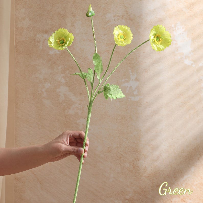 May include: A single artificial flower stem with three yellow-green poppy-like blooms and a bud. The stem and leaves are green. The word "Green" is written in cursive in the bottom right corner.