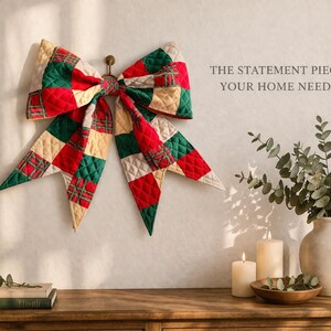 Może przedstawiać: Duża, pikowana kokarda w czerwono-zielono-kremową kratę wisi na ścianie. Kokarda jest centralnym punktem, z tekstem "THE STATEMENT PIECE YOUR HOME NEEDS" po prawej stronie. Drewniany st&oacute;ł mieści świece, wazon z zielenią i książki.