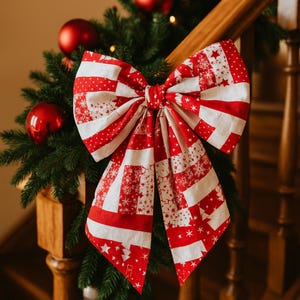 May include: A large Christmas bow with a red and white striped design, featuring snowflake and star patterns. The bow is attached to a garland of evergreen branches and red baubles, creating a festive holiday display.