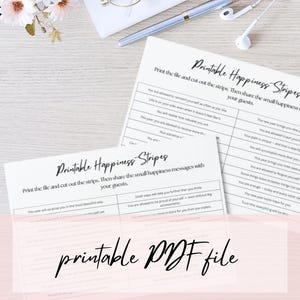 Könnte beinhalten: Druckbare PDF-Datei mit dem Text "Printable Happiness Stripes". Das Bild zeigt bedruckte Blätter mit positiven Affirmationen, einen Stift und Ohrhörer auf einer hellen Oberfläche. Die Blätter sind zum Zerschneiden in Streifen vorgesehen.