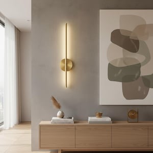 Puede incluir: Aplique de pared moderno con una tira de luz vertical e iluminada y una base circular. La lámpara es de metal dorado y está montada en una pared gris. Un complemento elegante para cualquier diseño de interiores.