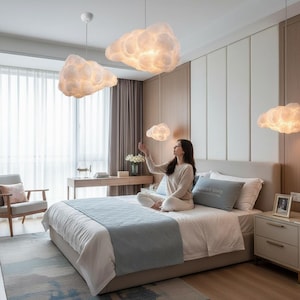 May include: A bedroom featuring cloud-shaped pendant lights. The lights are white and fluffy, resembling clouds. The room has a bed with a light blue blanket and a gray armchair. The walls are a light beige color.