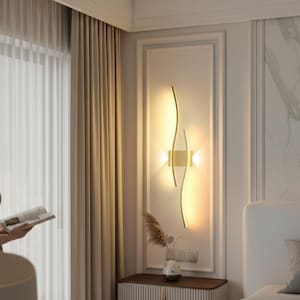 Peut inclure: Applique murale moderne avec une finition dorée, présentant un design incurvé avec deux sources lumineuses intégrées. L'applique est fixée sur un mur blanc, ajoutant une touche d'élégance à la pièce. La lumière chaude crée une ambiance chaleureuse.