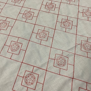 May include: White fabric with a repeating pattern of red embroidered squares. Each square contains a stylized floral design.