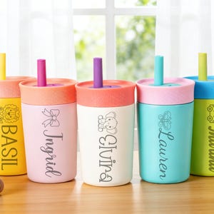 Puede incluir: Cinco vasos de colores con tapas y pajitas. Cada vaso tiene un color diferente, incluyendo amarillo, rosa, blanco, turquesa y verde. Los vasos est&aacute;n personalizados con nombres y gr&aacute;ficos decorativos, como un le&oacute;n, lazo, elefante, mariposa y coche.