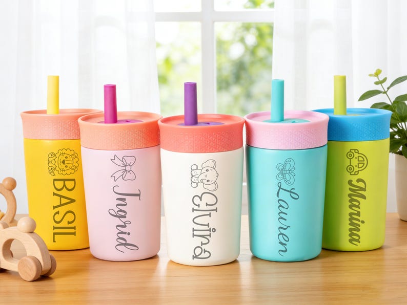 Puede incluir: Cinco vasos de colores con tapas y pajitas. Cada vaso tiene un color diferente, incluyendo amarillo, rosa, blanco, turquesa y verde. Los vasos est&aacute;n personalizados con nombres y gr&aacute;ficos decorativos, como un le&oacute;n, lazo, elefante, mariposa y coche.