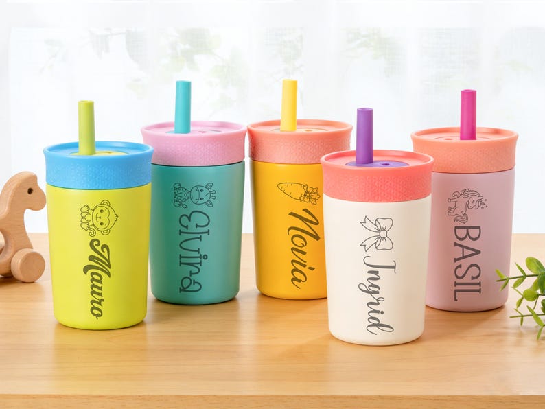 Puede incluir: Cinco vasos aislados de colores con tapas y pajitas. Cada vaso es de un color diferente, incluyendo amarillo, turquesa y rosa. Los vasos tienen nombres y peque&ntilde;as ilustraciones impresas, como un mono, una jirafa, una zanahoria, un lazo y un unicornio.