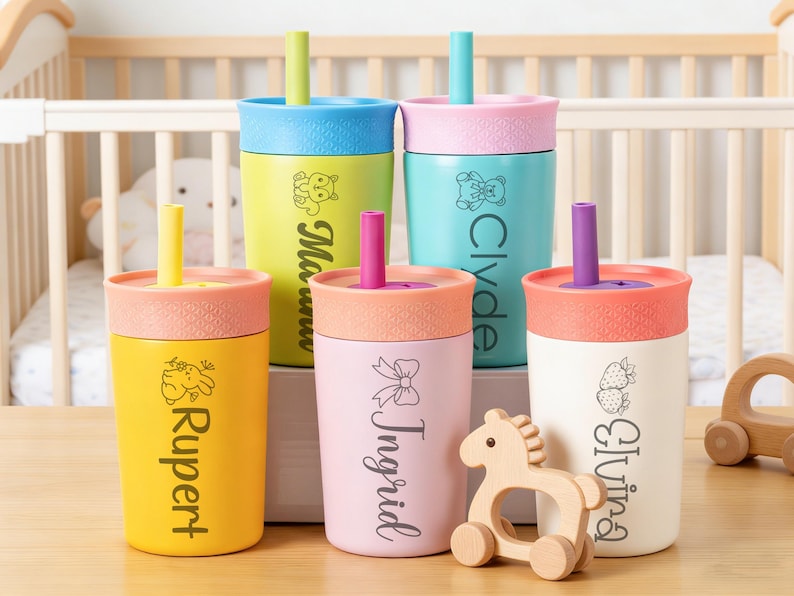Puede incluir: Una colecci&oacute;n de coloridas tazas para beb&eacute;s con tapas y pajitas. Cada taza es de un color diferente, incluyendo amarillo, rosa, azul y blanco, y presenta un nombre y un peque&ntilde;o gr&aacute;fico. Un caballo de juguete de madera est&aacute; al lado de las tazas.