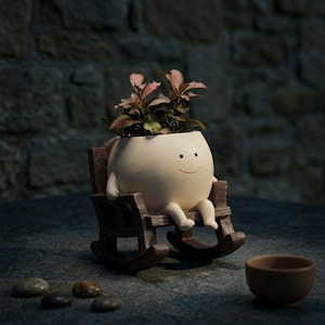 Alt Text: A whimsical cream-colored round face planter with a simple painted smile, sitting relaxed in a miniature brown wooden rocking chair. The cute character pot has small legs dangling down and is holding a vibrant pink and green fittonia nerve plant on a rustic wooden table.
