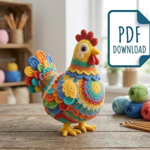 Puede incluir: Un gallo de ganchillo colorido con cuerpo amarillo, cresta y barbilla rojas y cola multicolor. El gallo tiene un diseño detallado y texturizado con varios tonos de azul, naranja y verde. La imagen incluye un gráfico de "PDF DOWNLOAD".