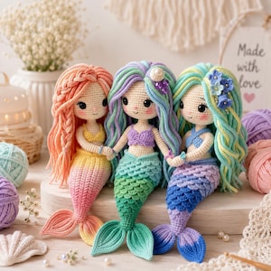 May include: Three handmade crochet mermaid dolls with yarn hair and detailed tails. The left doll has peach hair and a yellow-to-pink tail. The centre doll has purple-green hair and a green tail. The right doll has blue-green hair and a blue-purple tail.