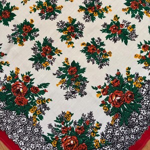 Könnte beinhalten: Eine weiße Blumentischdecke mit einem sich wiederholenden Muster aus roten Rosen, gelben Blumen und grünen Blättern. Der Rand hat ein schwarz-weißes Blumendesign mit rotem Besatz. Die Tischdecke ist aus gewebtem Stoff.