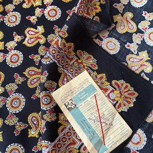 Peut inclure: Tissu bleu marine foncé à motifs cachemire avec des motifs floraux et en forme de goutte d'eau rouges, jaunes et blancs. Une étiquette vintage avec du texte en langue étrangère est attachée. Le tissu est plié.