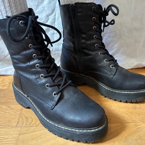 May include: A pair of black leather combat boots with a lace-up design and a chunky sole. The boots have a side zipper and are approximately 6 inches in height.