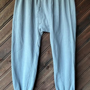 Puede incluir: Pantalones de chándal de color azul claro con cintura elástica y puños acanalados en los tobillos. La prenda incluye una abertura vertical en el panel frontal y está confeccionada con una tela de color sólido con textura suave y mate.
