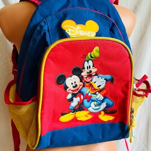 May include: A blue and red backpack featuring a graphic print of Mickey Mouse, Goofy, and Donald Duck on the front pocket. The bag includes a yellow mesh side pocket, a top handle, and a yellow-bordered front compartment with the Disney logo.