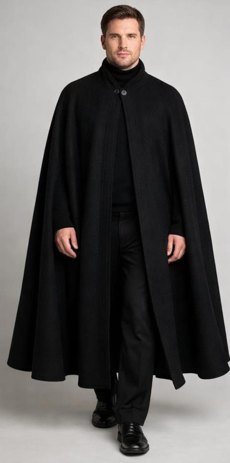 May include: A long, black cape with a high collar and two buttons. The cape is worn over a black turtleneck and black pants. The person is wearing black shoes. The overall look is formal and elegant.