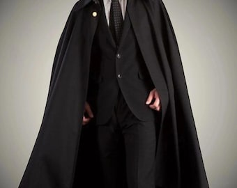 May include: A black cape with a button closure, worn over a black suit, white shirt, and black tie. The cape has a wide collar and a gold-colored button. The suit has a two-button closure.