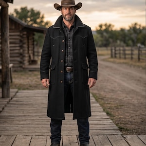 May include: A black wool duster coat with a brown leather collar and trim. The coat features four front pockets and a button-down closure. The person is wearing a brown cowboy hat, a plaid shirt, blue jeans, and brown leather boots.
