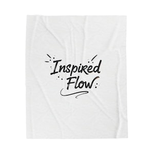 May include: White blanket with the words "Inspired Flow" in black script. The text is centered and has decorative elements around the words. The blanket has a slightly wrinkled texture.