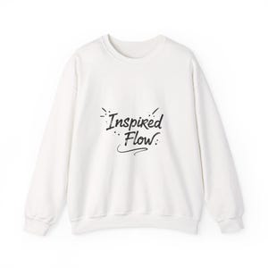 Op de afbeelding: Een witte crew neck sweatshirt met lange mouwen. De voorkant van de sweatshirt heeft de tekst "Inspired Flow" in een zwarte, handgeschreven lettertype. Het ontwerp bevat decoratieve elementen rond de tekst.
