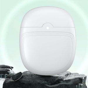 May include: A white, oval-shaped product, possibly a container or device, with a smooth, glossy finish. The design features a curved top with a small indentation and a subtle light. The product is set against a blurred, light green background and rests on a dark, textured surface.