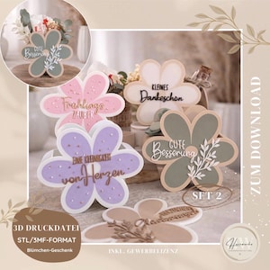 Puede incluir: Un conjunto de adornos con forma de flor en colores pastel, incluyendo rosa, morado y verde. Cada flor tiene una frase en alemán, como "Gute Besserung" y "Frühlingszauber". El conjunto incluye una etiqueta "SET 2".