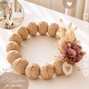 Puede incluir: Un anillo decorativo circular compuesto por múltiples cáscaras en forma de nuez de color tostado dispuestas en bucle. Un lado presenta un grupo de flores secas beige y malva, una pequeña etiqueta circular blanca con un corazón y el texto 3D-Druckdatei STL / 3MF-Datei.