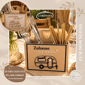 May include: A beige rectangular cutlery organiser with multiple compartments, featuring a black graphic of a camper trailer and the German text "Zuhause auf Rädern". The organiser includes a heart cutout handle and holds silver and gold utensils.